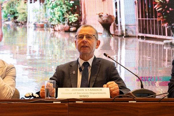 Man sitting at a table in front of screen showing a flooded area.
