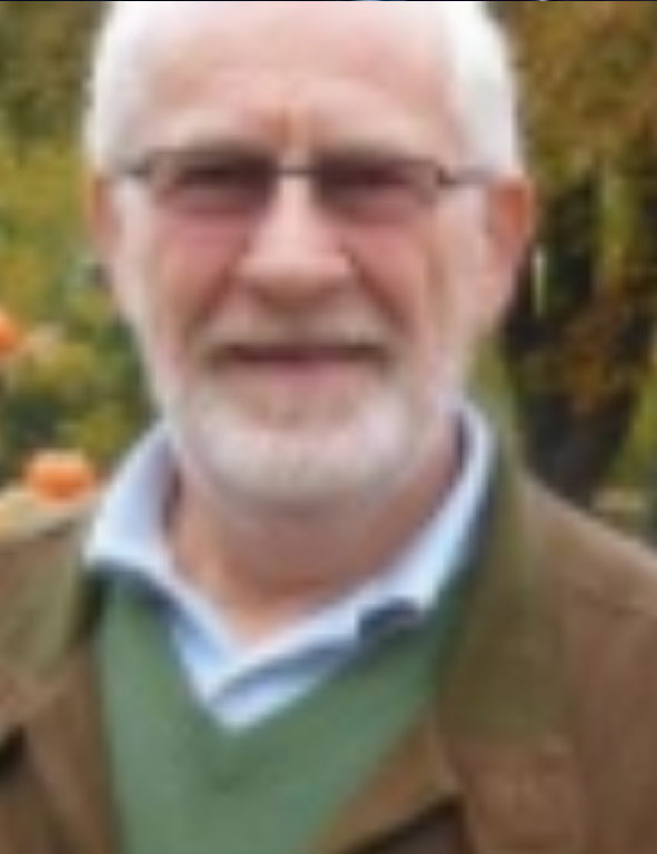 An older man wearing glasses and a green jacket.