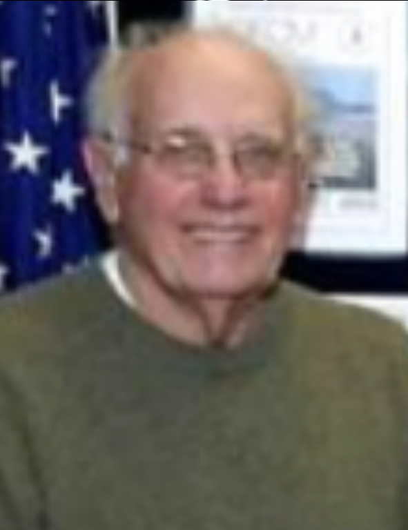 An older man smiling in front of an american flag.