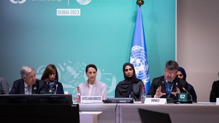 A group of people sitting at a table in front of a flag.