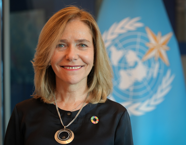 A woman smiling in front of a flag.