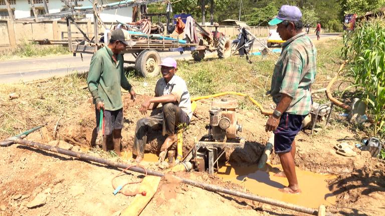 A group of men are working on a water well in a dirt road.