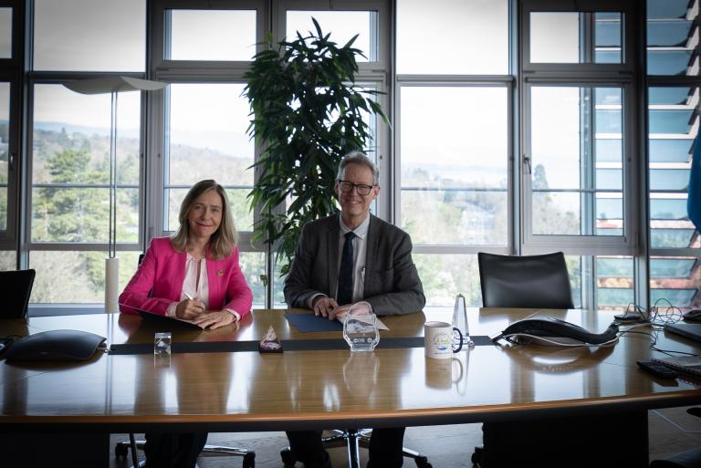 Two professionals seated at a conference table in a well-lit office with a view of the outdoors.