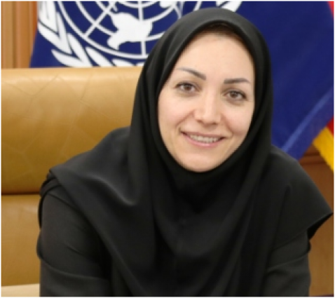 A woman in a black hijab smiling in front of flags.