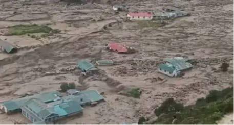Aerial view of damaged houses scattered in a muddy landscape after a flood.