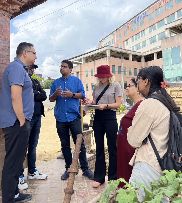 A group of people stand and talk outside a building, with one person taking notes.
