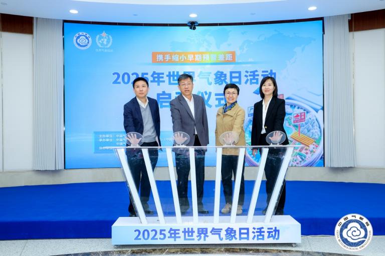 Four people stand on a stage with hands on a podium at the 2025 World Meteorological Day event, with a banner in the background.