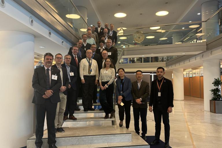 A group of people in business attire poses for a photo on a staircase inside a modern office building with glass railings.