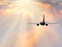 Airplane flying towards a bright, cloudy sky with beams of sunlight shining through the clouds.