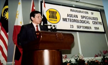 A man stands at a podium speaking at the inauguration of the ASEAN Specialised Meteorological Centre on September 23, 1994, with national flags and a sign in the background.