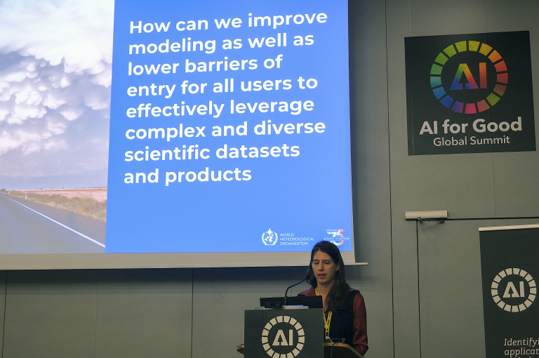 A woman speaks at a podium during the AI for Good Global Summit, with a large screen displaying a slide about improving modeling and access to scientific datasets.