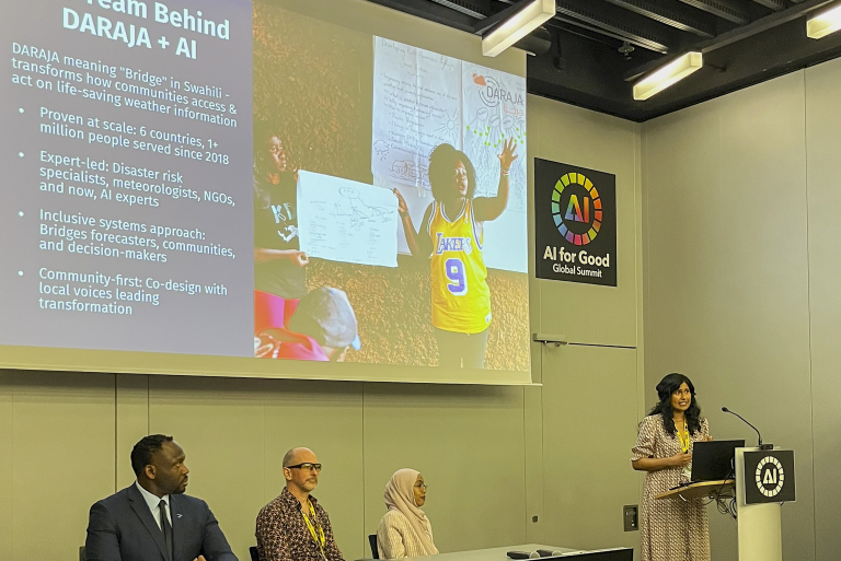 A woman presents at a conference podium beside three seated panelists, with a slide about the DARAJA AI initiative displayed on a screen behind them.