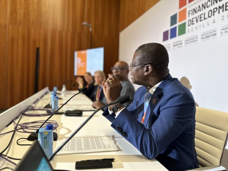 A panel of speakers sits at a conference table with microphones, participating in the Financing for Development event in Sevilla 2022.