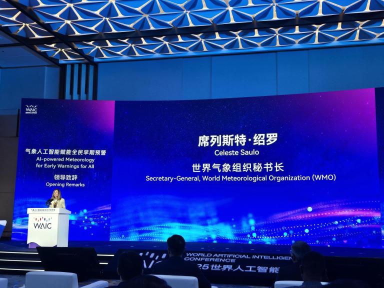 A woman stands at a podium giving opening remarks at the World Artificial Intelligence Conference, with a large screen displaying information about Celeste Saulo from the WMO.