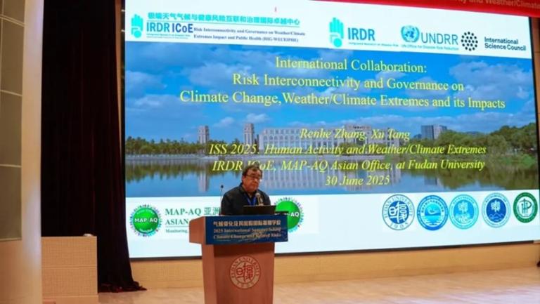 A speaker stands at a podium in front of a large screen displaying a conference presentation on climate change, weather extremes, and international collaboration.