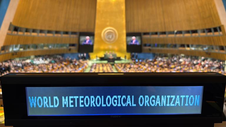 A digital sign reading "World Meteorological Organization" in the foreground, with a large assembly and speakers at a United Nations auditorium in the background.