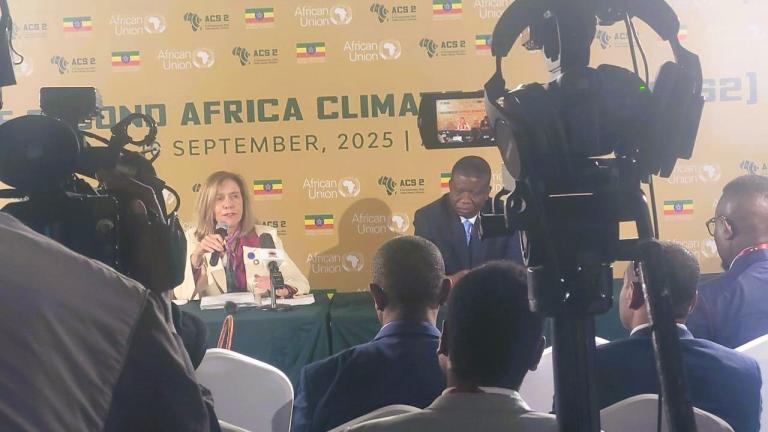 A woman and a man speak at a press conference table during the 2025 Africa Climate event, with cameras and attendees focused on them.