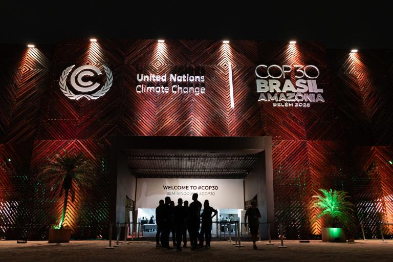 A group of people stands outside the entrance to a building with signs for United Nations Climate Change and COP30 Brasil Amazônia Belém 2025.