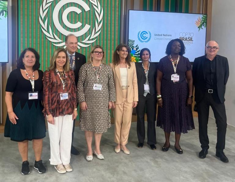 Eight people stand in a row at a United Nations Climate Change event, with official logos and signage visible in the background.