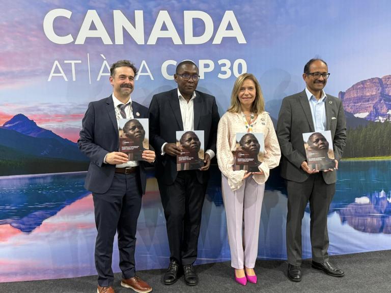 Four people in business attire stand in front of a backdrop reading "CANADA AT À LA COP30," each holding a report with a child's face on the cover.