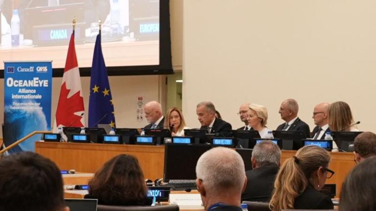 Panel of officials seated at a conference table, with Canadian and EU flags behind them, and an “Ocean Eye” banner visible on the left side of the image.
