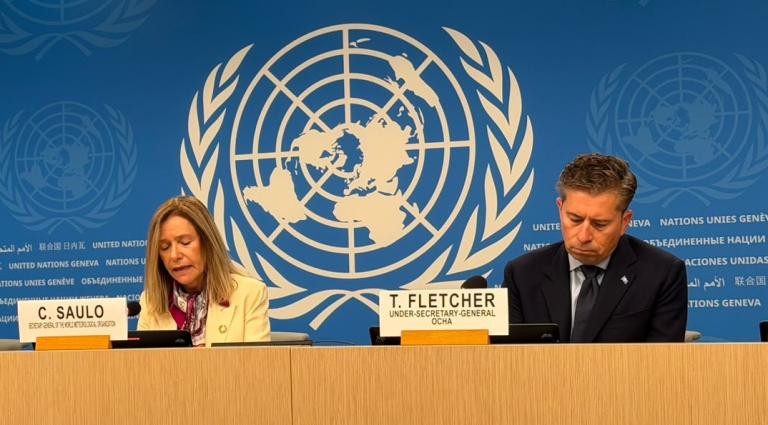 Celeste Saulo and Tom Fletcher sit at a table in front of a United Nations backdrop with nameplates identifying them.