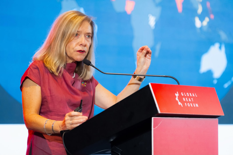 A woman speaking at a podium labeled “Global Heat Forum” with a world map in the background.