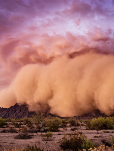 A cloud of dust in the desert with mountains in the background.