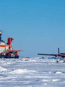 Two small planes on the ice next to a large ship.