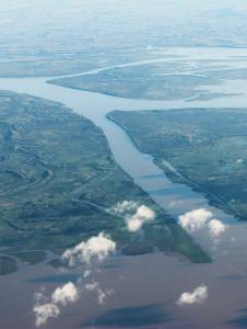 Aerial view of a meandering river with adjacent floodplains and scattered clouds casting shadows below.