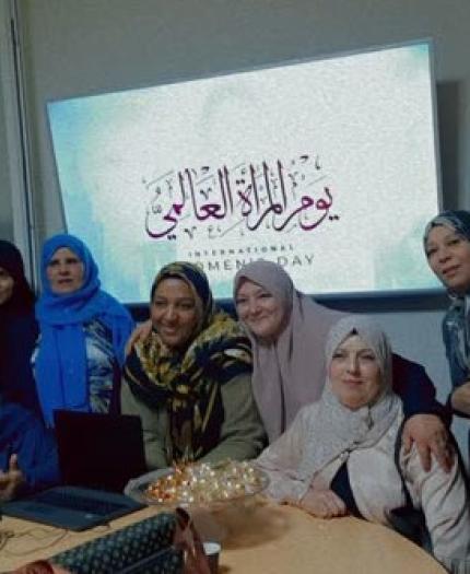 Group of women posing together in a room with a screen displaying text in the background for an event or celebration.
