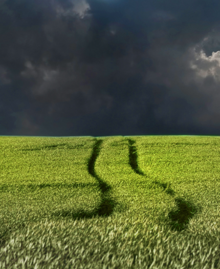 A green field with tire tracks under a dark, stormy sky.