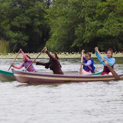People paddling two canoes on a calm lake surrounded by lush greenery.