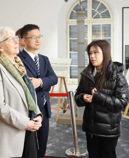 Four people stand together in a museum or gallery, listening to a guide explain framed photographs on the wall.