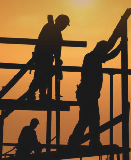 Three construction workers are silhouetted against an orange sunset sky as they work on a building framework.
