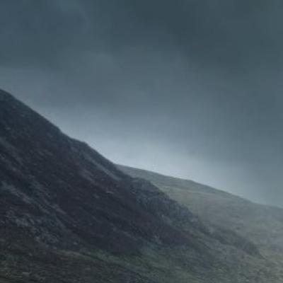Dark, overcast sky above a sloping, rocky hillside with patches of grass and sparse vegetation.