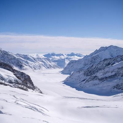 Snow-covered mountains and a glacier under a clear blue sky, with rugged peaks and a wide valley extending into the distance.