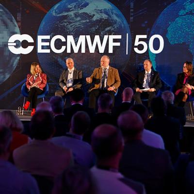 A panel of six people speaks on stage at an ECMWF 50th anniversary event, with an audience seated in front and large screens showing Earth in the background.