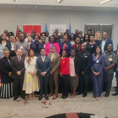 A large group of professionally dressed people pose for a group photo in a conference room, with banners in the background.
