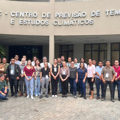 A group of people poses for a photo in front of the CPTEC - Centro de Previsão de Tempo e Estudos Climáticos building.