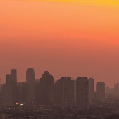 Silhouetted city skyline with numerous high-rise buildings under an orange and yellow sunset sky.
