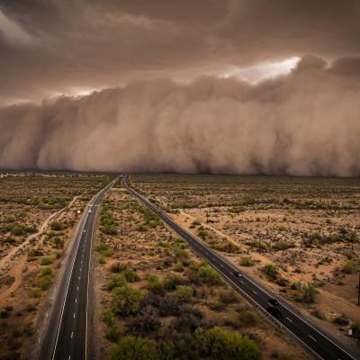 A massive dust storm approaching a highway running through a desert landscape.