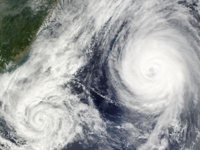 Satellite image of two large cyclones in the ocean near a landmass, with swirling cloud patterns visible.