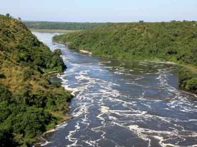 A wide river with swirling water flows between green, tree-covered hills under a clear sky.