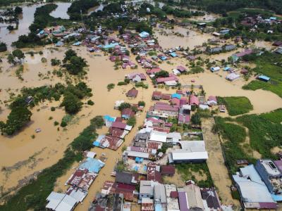 Aerial view of a flooded town with numerous buildings partially submerged in muddy water and surrounding areas also impacted by the flood.