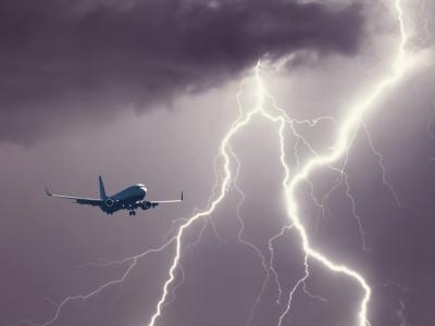 A commercial airplane flies near a large lightning strike in a dark, cloudy sky.