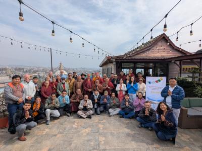 A group of people pose for a photo on a rooftop with string lights, a city view, and a banner that reads "HIA Daily." Most of them have their palms together in a greeting gesture.