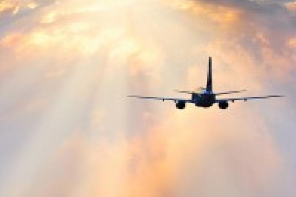 Airplane flying towards a bright, cloudy sky with beams of sunlight shining through the clouds.